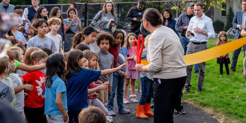 Students stand with the principal preparing to cut the ribbon on the playground