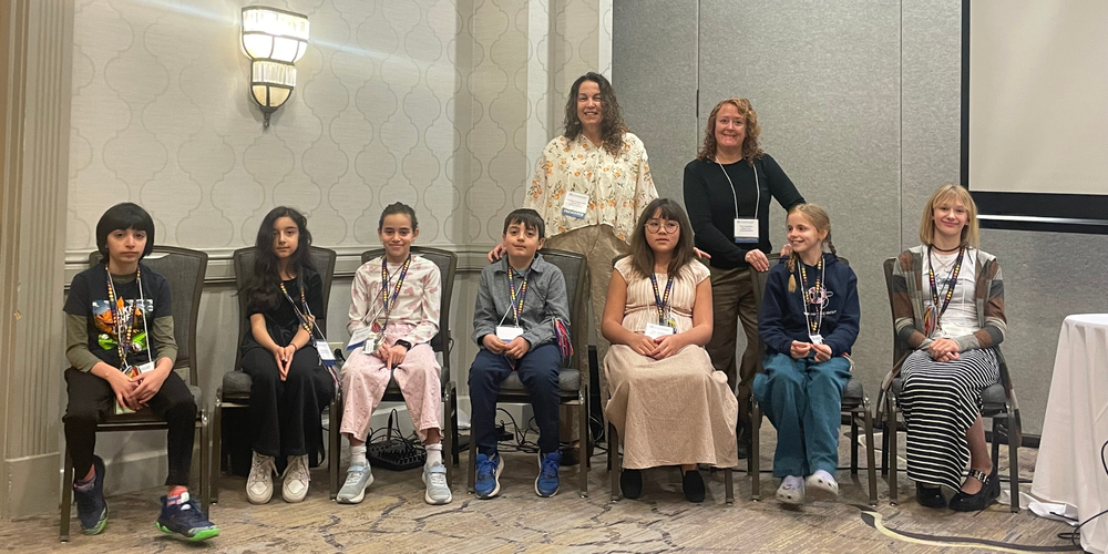 Seven students from Northeast elementary seated in a line at a conference. 