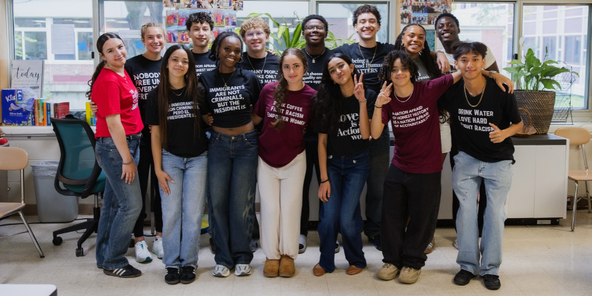 Students wearing custom shirts stand and pose for a group photo in a classroom