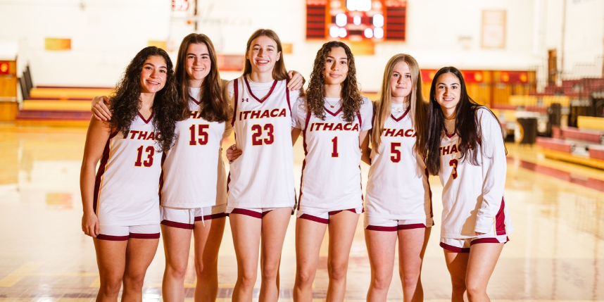 Six female student-athletes pose on a basketball court wearing their uniforms
