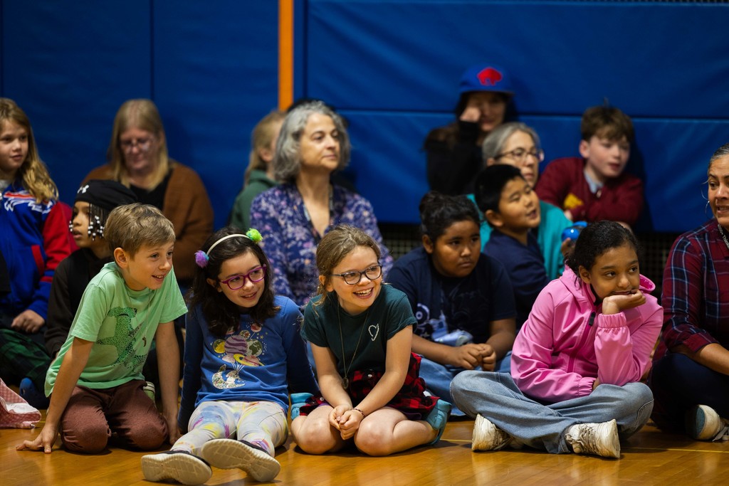 Students sitting on the gym floor smiling 
