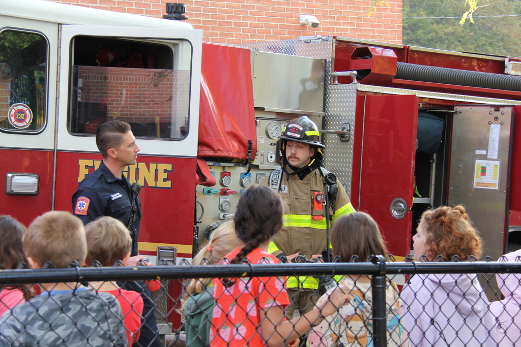 Two Ithaca fire fighters engaging with students outside of Fall Creek. They are standing in front of a fire truck. 