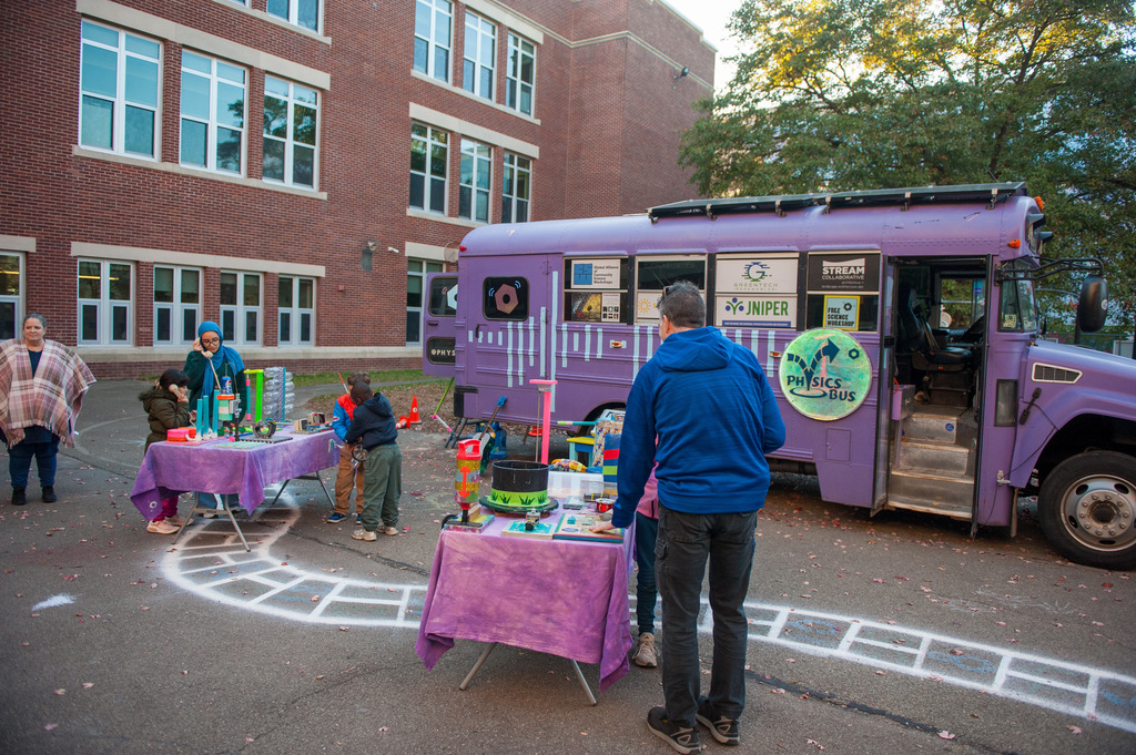 Students at tables outside the physics bus playing at different stations
