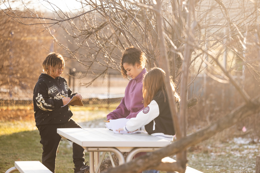 Three students gathered around a table writing in their journals. 