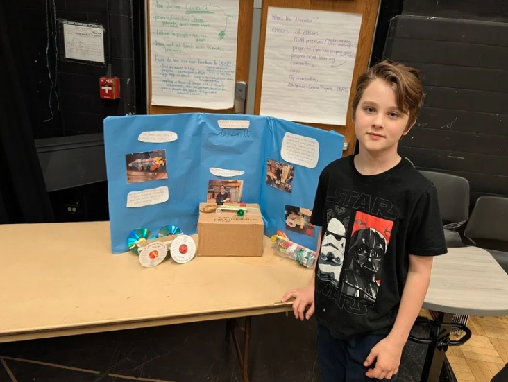 An LACS 6th-grader stands in front of their yellow poster board at the science fair
