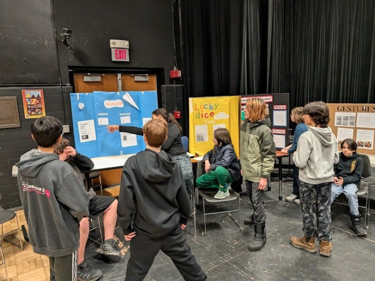 A group of students gathered around a poster board at the 6th grade science fair at LACS
