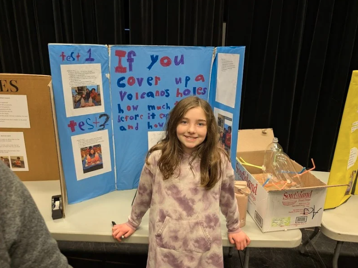 An LACS 6th-grader stands in front of their yellow poster board at the science fair
