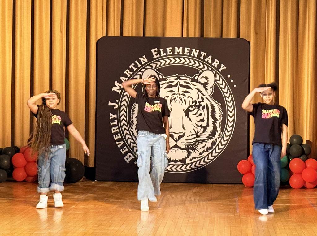 Three bjm students dancing on stage in front of the BJM logo