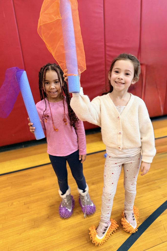 Two bjm students in the gym holding up noodles with scarves on them