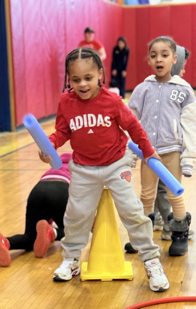 Student in BJM gym holding two noodles. 