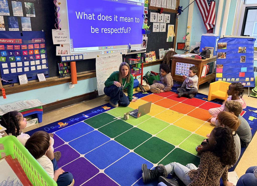 Classroom at BJM with students sitting on the ground in a circle with a teacher leading a lesson. 
