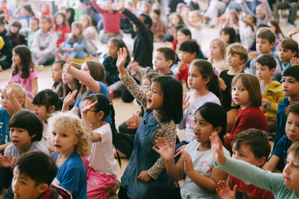 Cayuga Heights students sitting on the floor of the cafeteria watching the musical and waving.