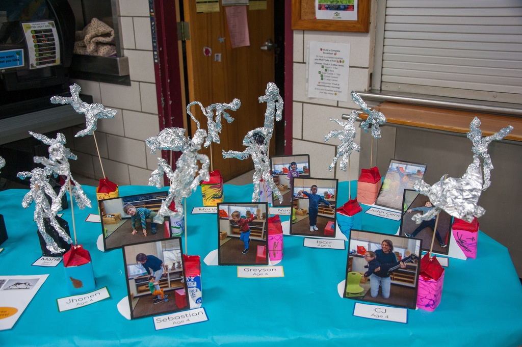 A table displays aluminum foil sculptures with photos. A blue tablecloth covers the table, and several small pictures are arranged.