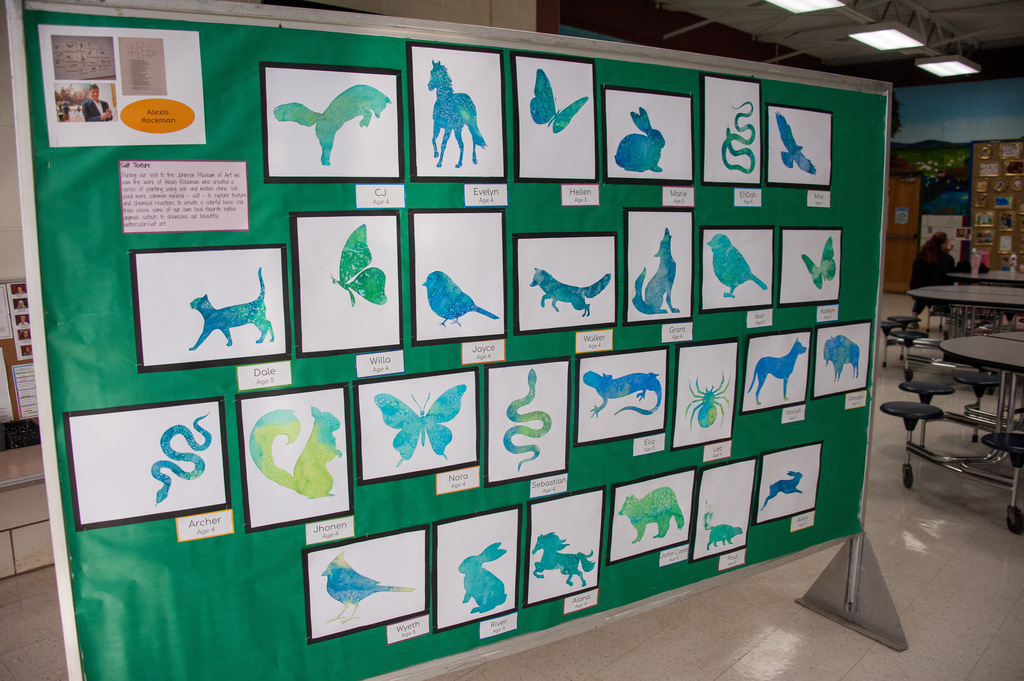 Display of various animal silhouettes in blue and green on a green background. Several tables and chairs are visible in the background.