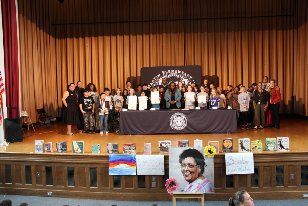 People on stage at an event with a banner behind them. A person stands out in a photo.