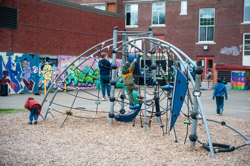 Playground with climbing structures. Four children play on it. Graffiti on a brick wall.