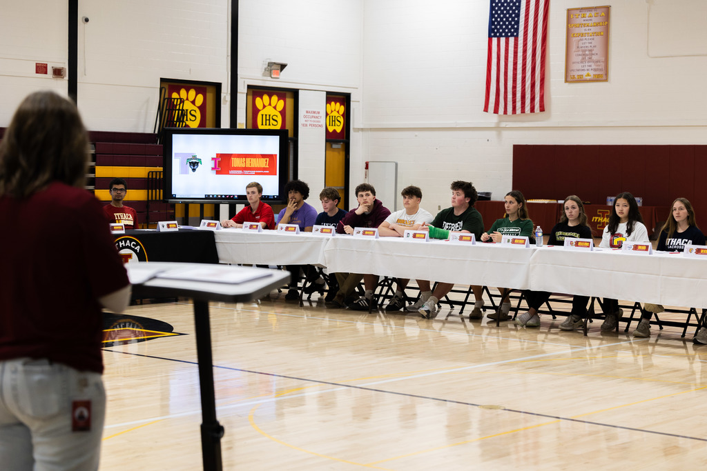 Indoor court with a monitor, a person standing at a podium, and a table with seated people.