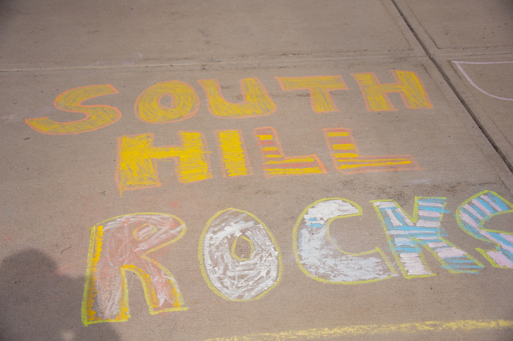 Sidewalk with chalk writing "SOUTH HILL ROCKS" in various colors. A shadow is cast on the left.