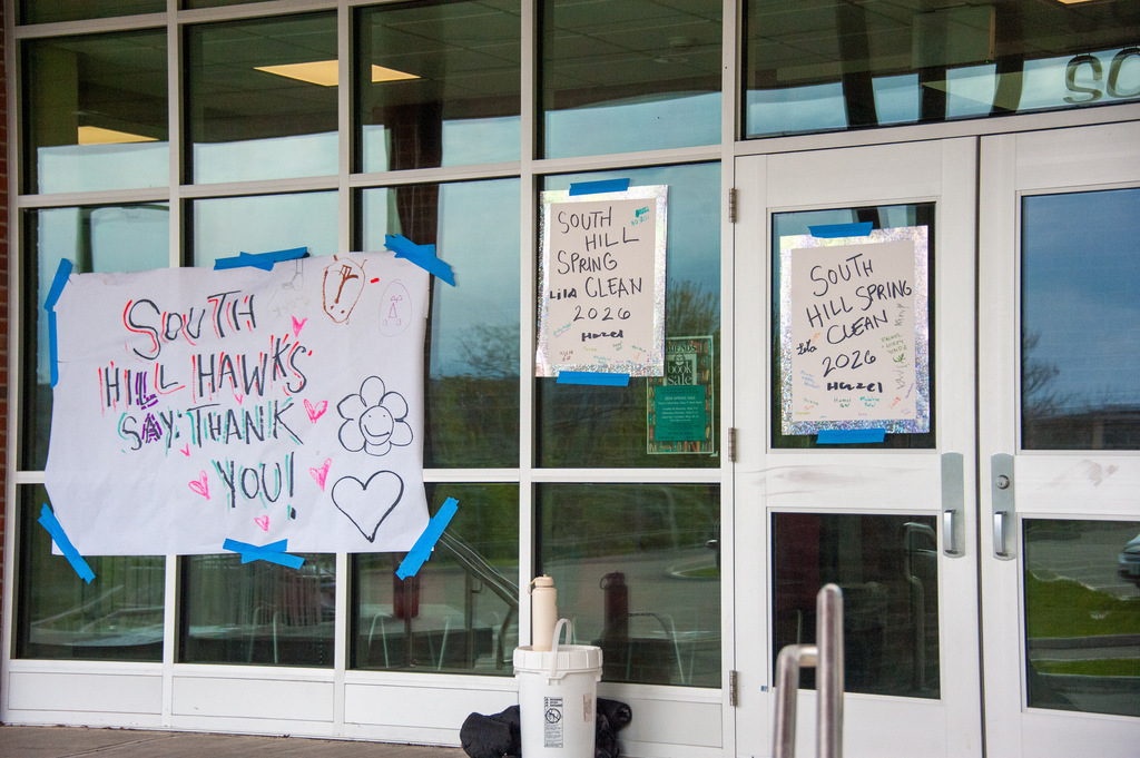 Three posters taped to a glass door, one with pink hearts, one with green text, and one with blue tape.