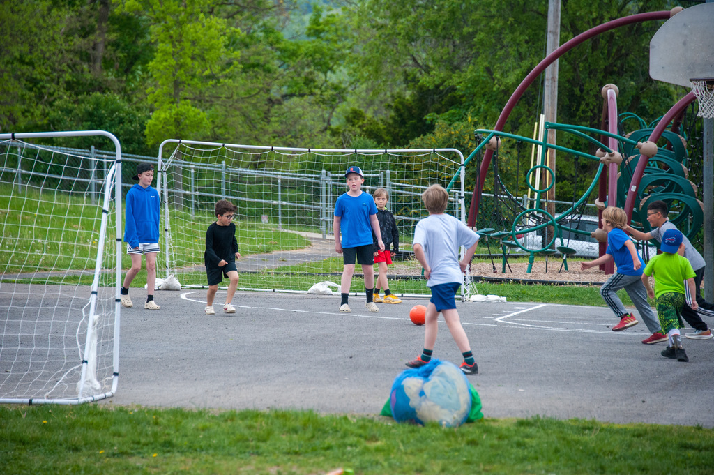Several children play a game with a ball on a playground, near a basketball goal.
