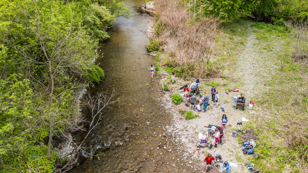 Group of people in a river valley. Some are in the river while others sit on the bank.
