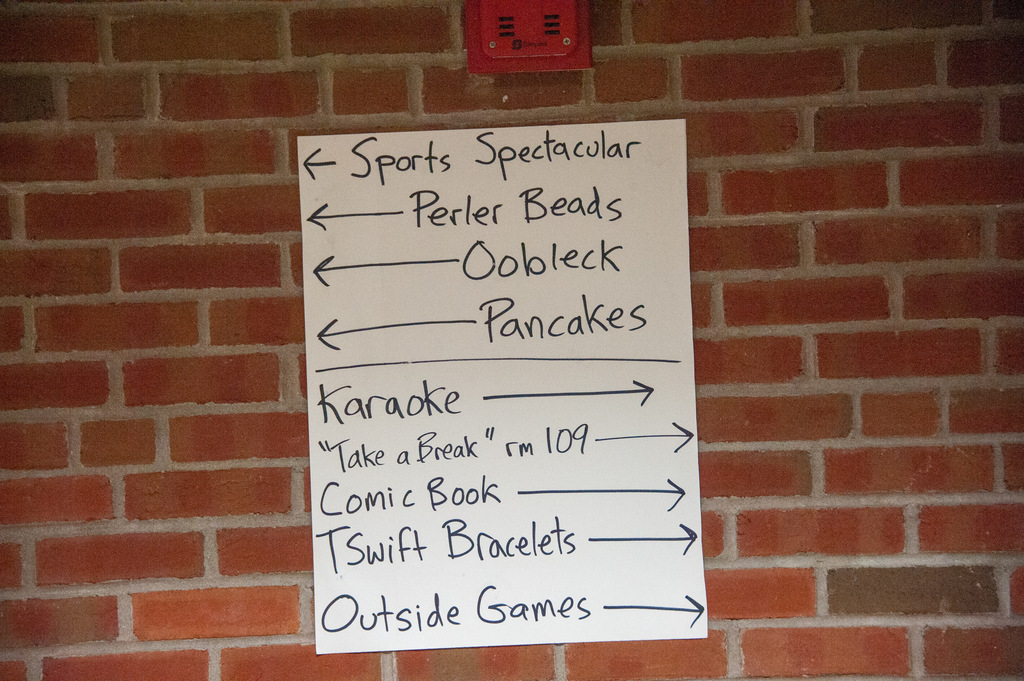 A white board pinned to a brick wall with arrows pointing to various activities like Sports Spectacular, Karaoke, and Outside Games.