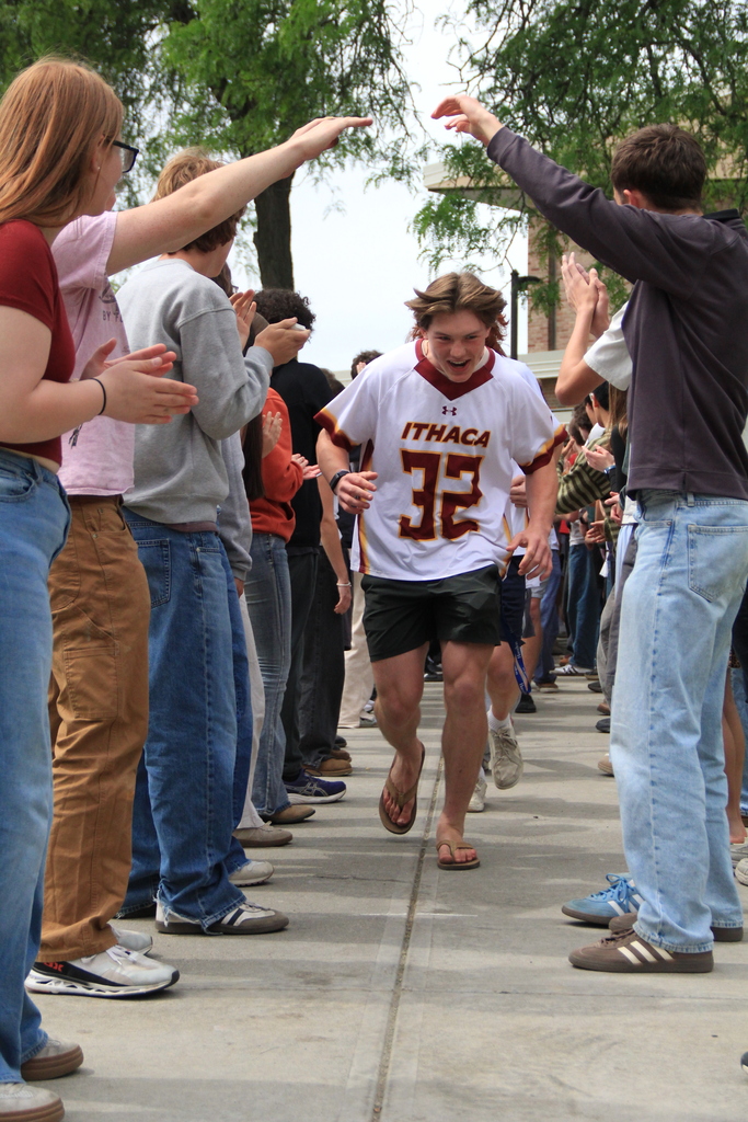 A runner with the number 32 on his shirt runs through a crowd of people on a sidewalk.