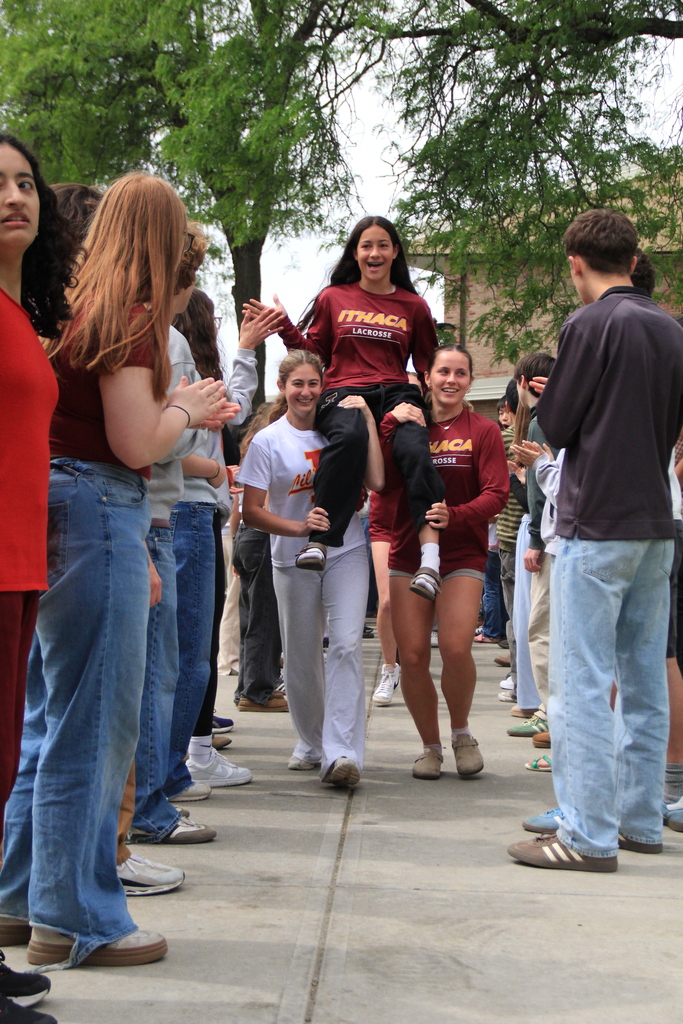 A group of people outdoors. One person is carried on another's shoulders. Some wear maroon shirts.