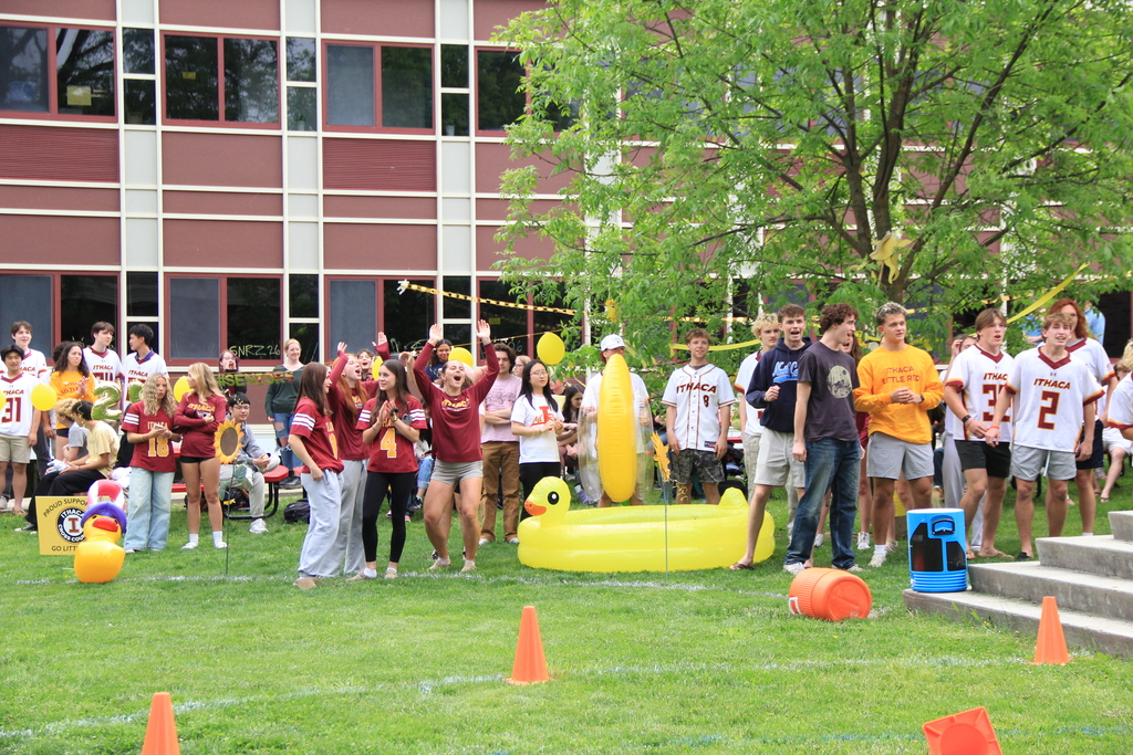A group of people on a lawn with inflatables and orange cones. Some wear maroon and white shirts.