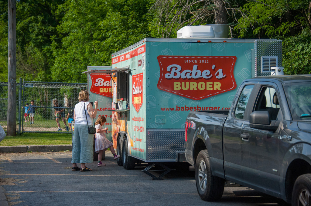 A food truck labeled Babe's Burger. A woman and child stand in front of it. A pickup truck is parked to the right.