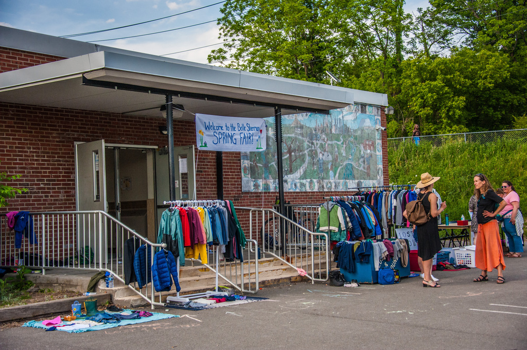 A brick building with a sign and a mural. People shop at an outdoor clothing sale.
