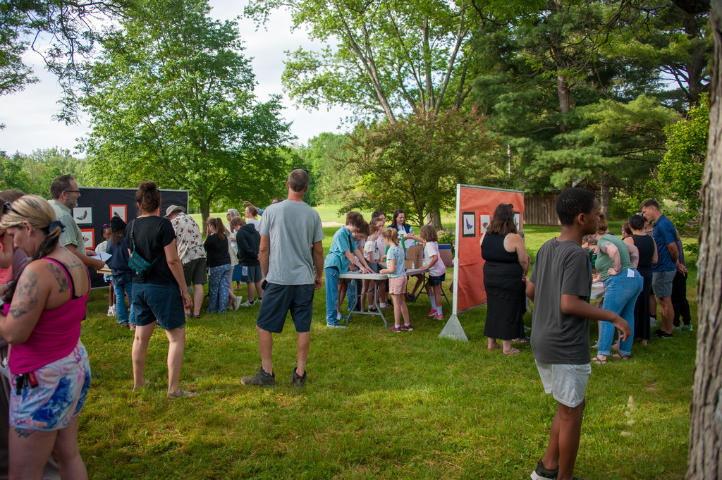 A group of people gathered in a park with tables and booths set up under trees.
