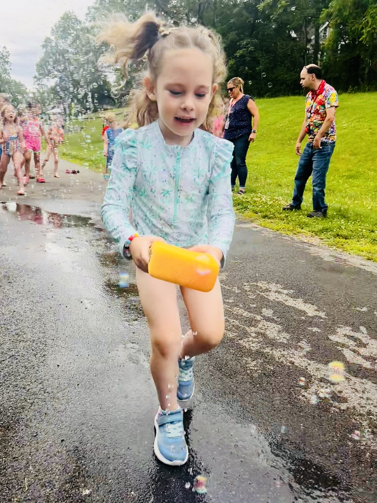 A young girl runs on a wet road, holding a yellow object and surrounded by a group.