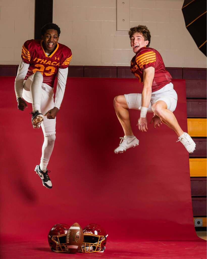 Two football players jump in air on red background. One wears red and white uniform, other red, white, and yellow.
