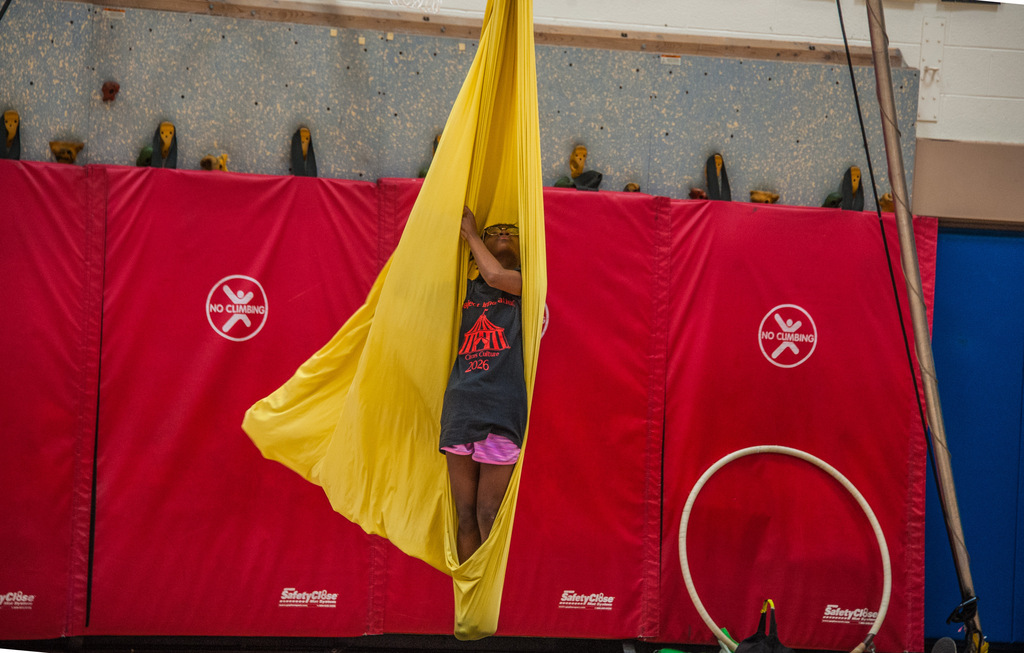 A child inside a yellow fabric hammock hanging from the ceiling, with red padded walls in the background.