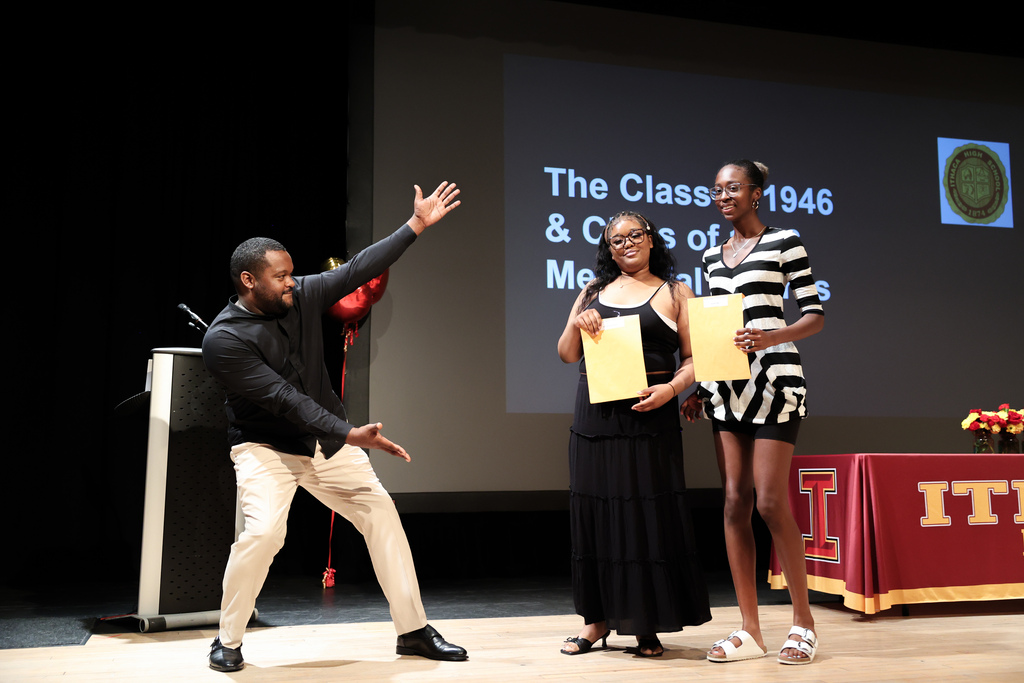 Teacher stands on stage presenting an award to two students.