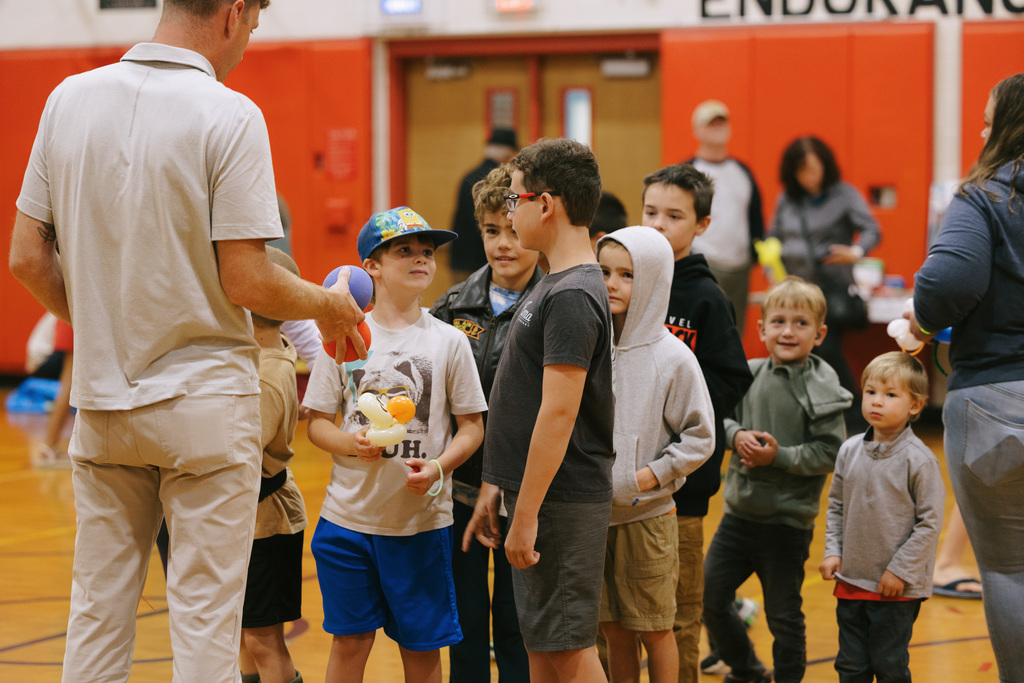 Principal Stephen hands a ball to a boy among a group of children inside a gym.