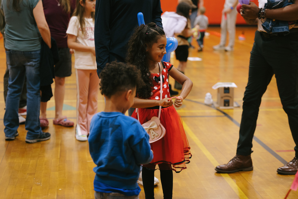 A child in a red and white polka dot dress and a young boy in a blue shirt interact at a school event.