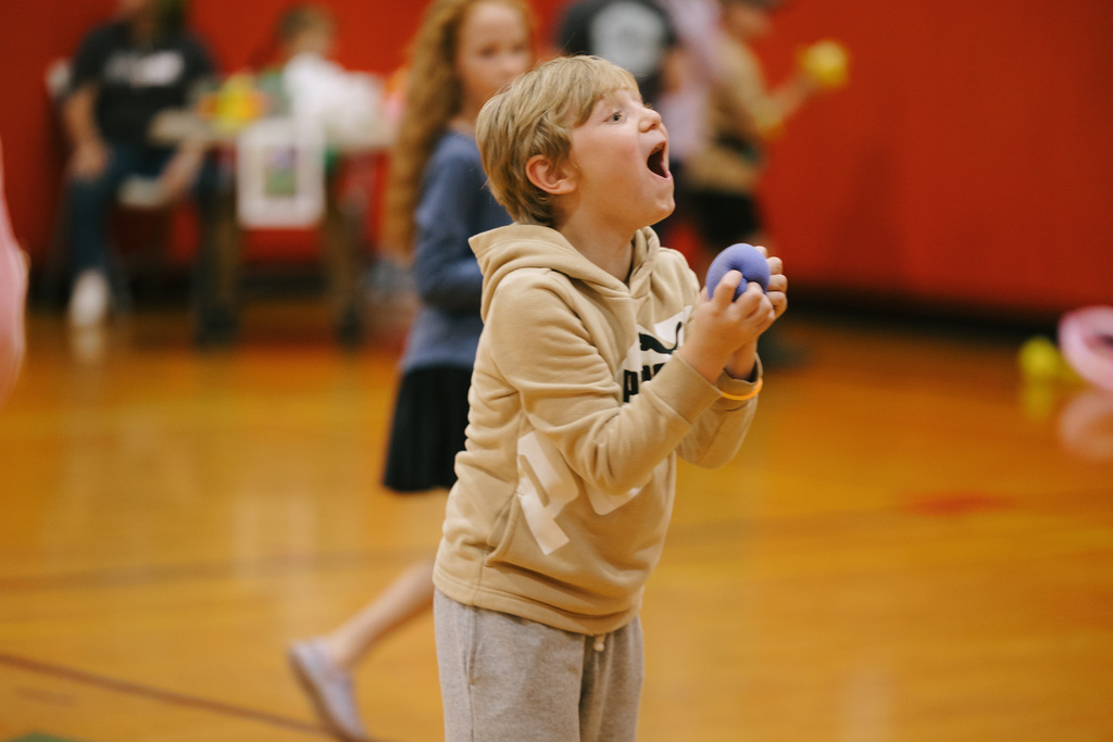 A child in a hoodie shouts while playing with a ball in an indoor court.