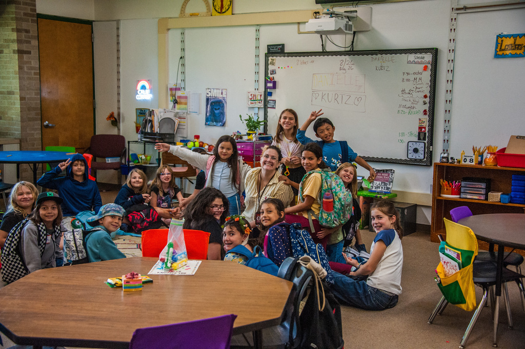 A classroom with children and adults. Some sit at a table and others stand and pose.
