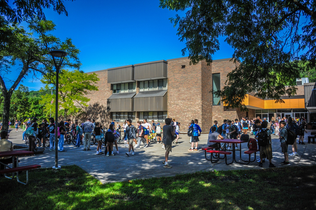 A crowd of students wearing backpacks gathered outside a brick building with a blue sky.