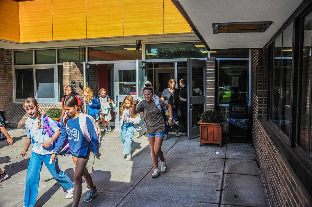 Several children in casual clothes walking through an entrance of a brick building with glass doors.