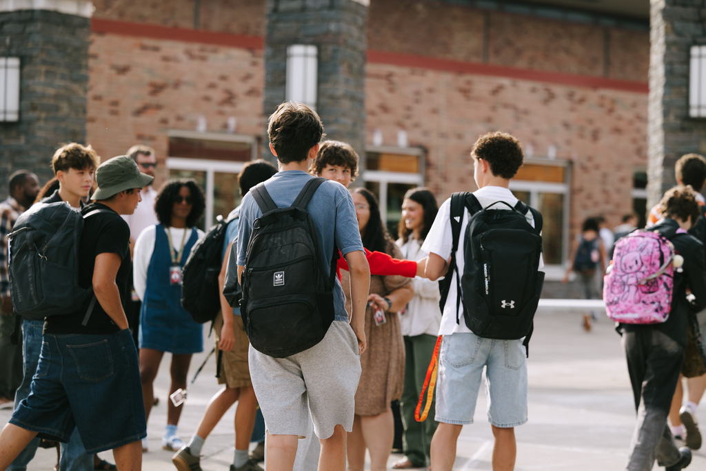 Various students in school attire, carrying backpacks, walk and converse in an outdoor area.
