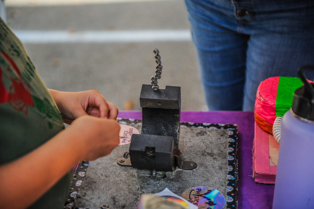 A child at a table shapes metal using a tool. Various items are on the table.