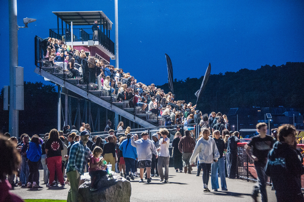 A large group of people in an outdoor area, some walking and others sitting on the steps of a stadium.