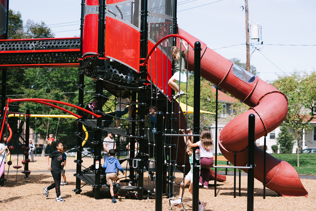 A playground with various climbing structures and a large red slide, with children playing on the equipment.