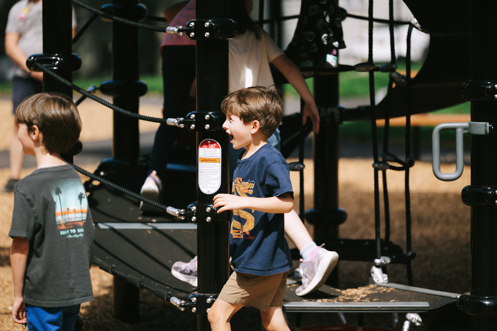 Two boys on a playground. One is climbing up a ladder while the other stands near a post.
