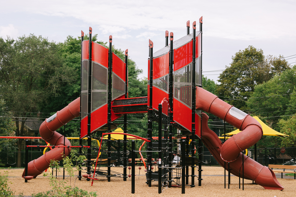 A playground with two large red slides, red-and-black vertical structures, and yellow canopy umbrellas.