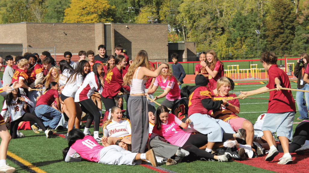 A group of individuals in red and white shirts engage in a team-building activity on a field.