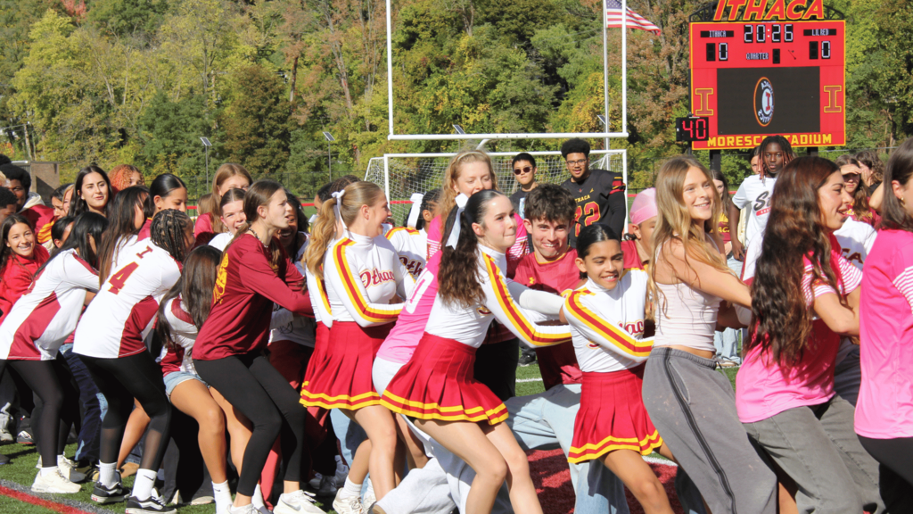 Cheerleaders in red and white uniforms playing tug of war, trees in the background.